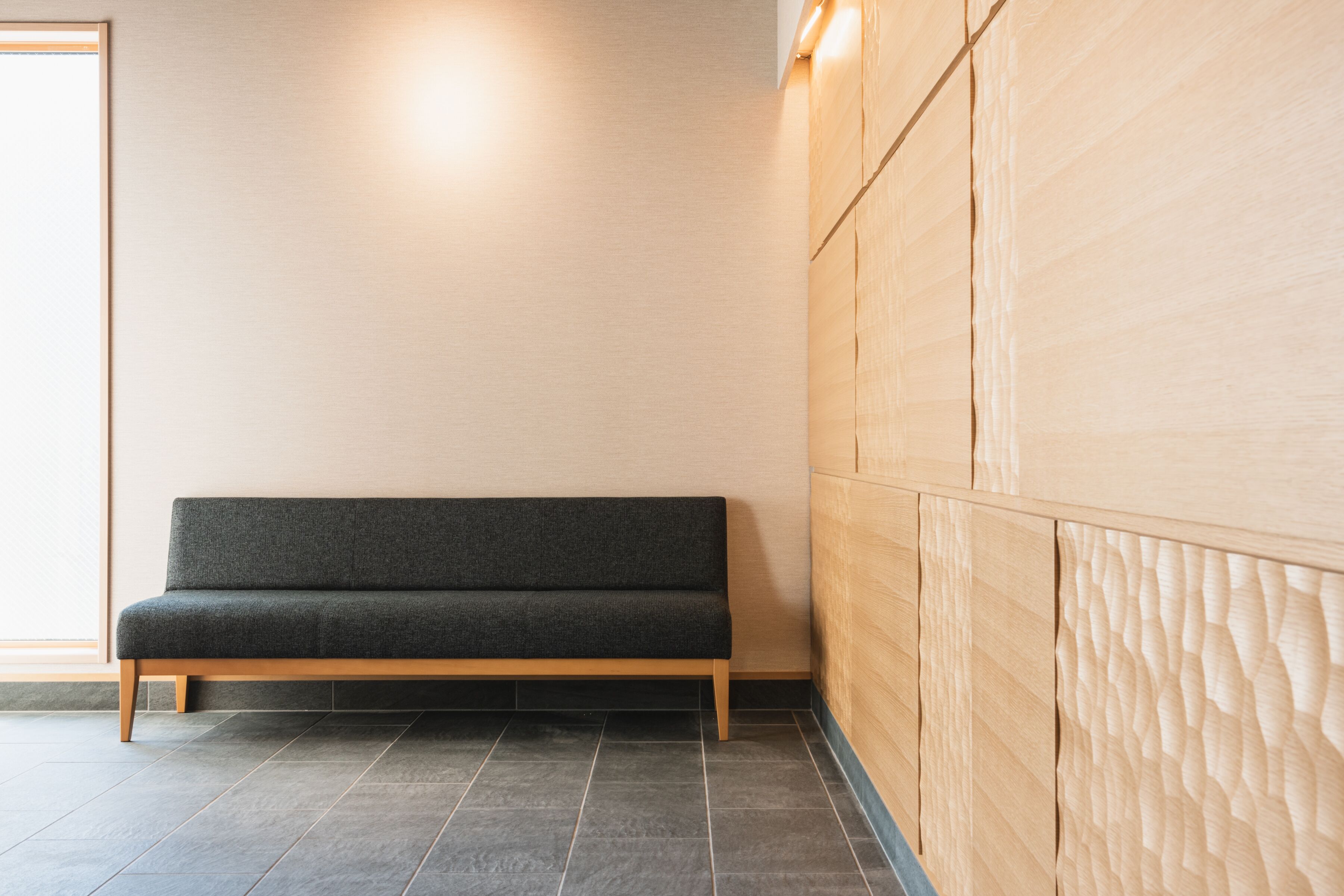 A minimalist room with a dark grey sofa, wooden panel wall, and tiled flooring.