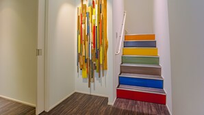 A modern interior with a wooden floor, a staircase with colorful steps, and a wall with vertical wooden planks. - Bond Base (Fukuoka)