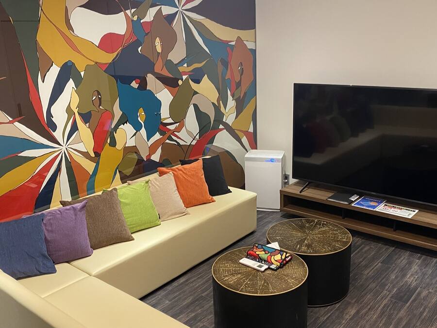 Un salon moderne doté d’un grand téléviseur à écran plat, d’un canapé beige agrémenté de coussins colorés et d’une fresque murale abstraite aux couleurs vives.