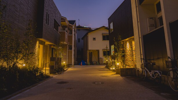 A narrow street flanked by multi-story buildings with balconies and outdoor lighting. - Bond Base (Fukuoka)