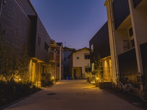 A narrow street flanked by multi-story buildings with balconies and outdoor lighting. - Bond Base (Fukuoka)