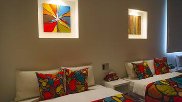 A hotel room with two beds, colorful abstract art on the walls, and a window with blinds.