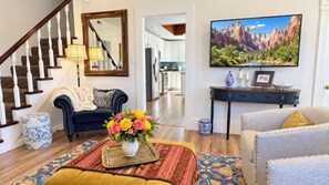 A living room with a sofa, a coffee table with a vase of flowers, a television, and a staircase.