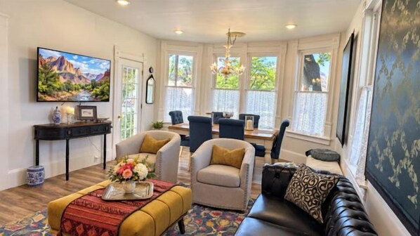 A living room with a sofa, chairs, a coffee table, and a television. There is a dining area with a table and chairs.