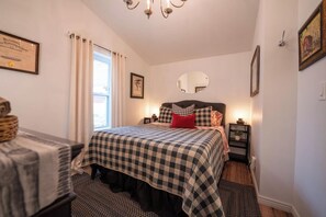 A bedroom with a bed, a bedside table, a lamp, a mirror, and a framed diploma on the wall.