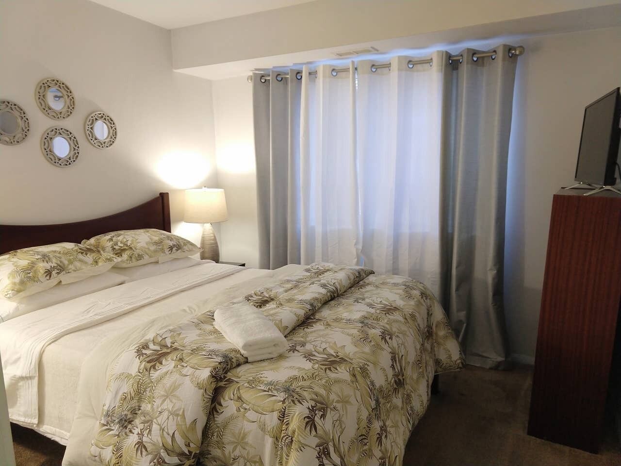 Ein Hotelzimmer mit Bett, Nachttisch, Lampe, Fernseher und Vorhang.