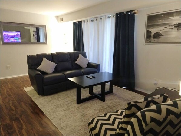 A living room with a black sofa, a coffee table, and a patterned armchair.