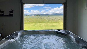 A hot tub with a view of a grassy field and mountains. - 35 MI to YNP | Private Hot Tub | Waterfront Access (Island Park)