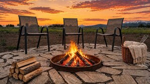 A fire pit with logs, three chairs, and a basket with a blanket. - 35 MI to YNP | Private Hot Tub | Waterfront Access (Island Park)