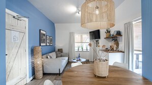 A living room with a wooden dining table, a sofa, a TV, and a large woven light fixture. - South Beach House 3 - Studio (Zandvoort)