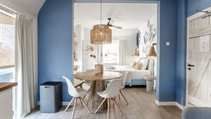 A modern room with a round dining table, white chairs, and a ceiling fan. - South Beach House 3 - Studio (Zandvoort)