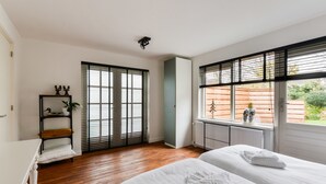 Ein Schlafzimmer mit zwei Betten, Holzboden, Heizkörper und einem Fenster mit Jalousien.