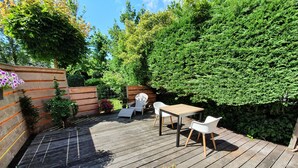 Eine Holzterrasse mit Tisch und Stühlen, umgeben von Grünpflanzen und einem Holzzaun.