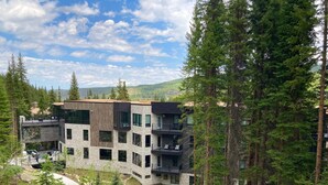 Un edificio moderno a più piani con balconi, immerso in una fitta foresta e affiancato da un sentiero sinuoso.