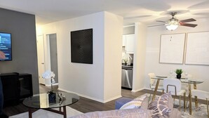A modern living room with a gray sofa, a glass coffee table, and a dining area with a glass table and chairs. - Reflections - 2bdr condo in Central Raleigh (Raleigh)