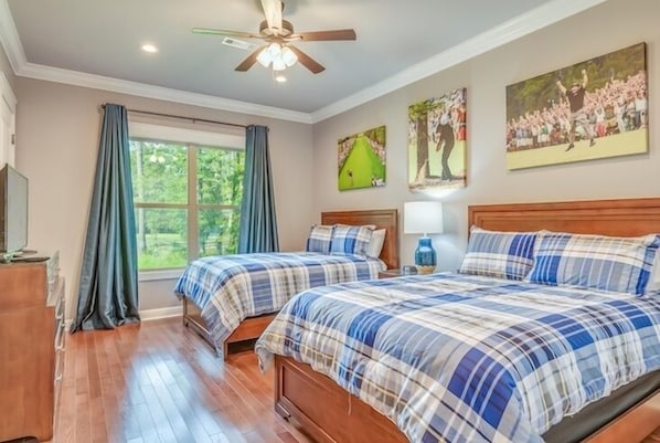 A bedroom with two beds, a ceiling fan, a window with curtains, and wall art.
