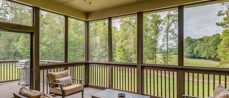 A covered outdoor area with a wooden deck, a ceiling fan, and a view of a wooded area.