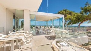 An outdoor dining area with glass walls, white furniture, and a view of the sea. - Hotel Perla Saracena - Villette con Giardino (Torre Pali)