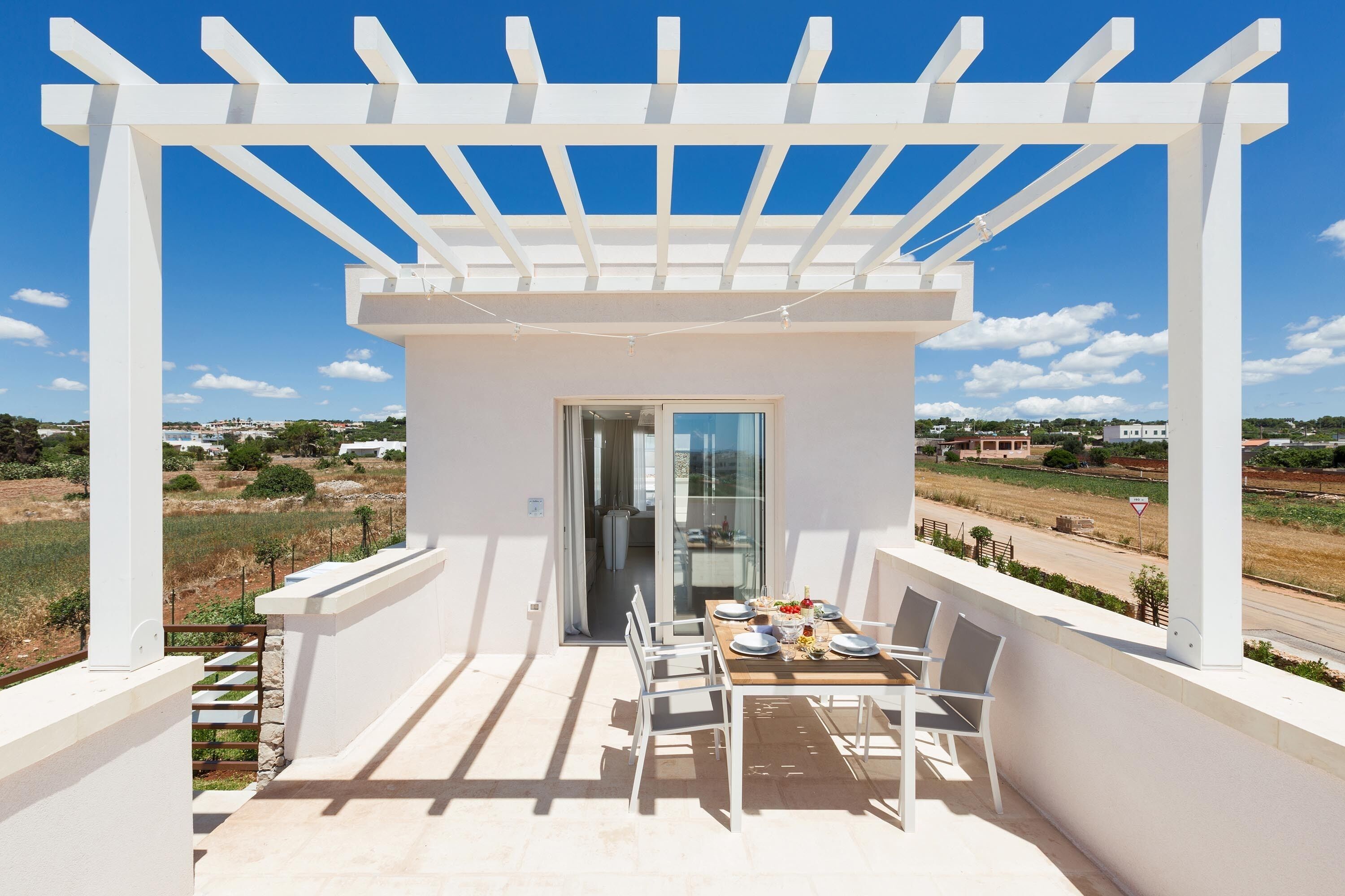Un balcon agrémenté d’une pergola, une table dressée pour le repas et une vue sur la campagne.