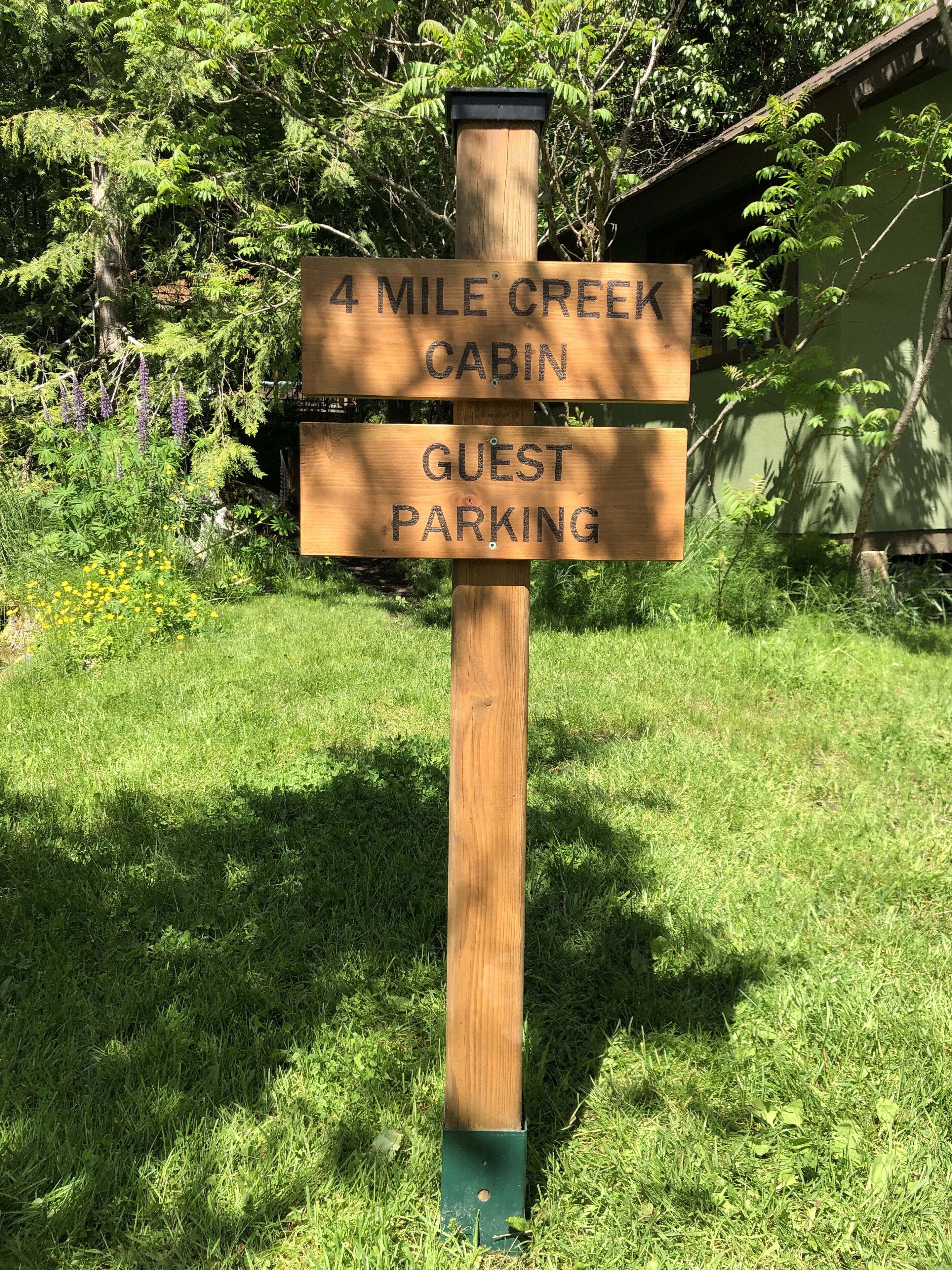 Un panneau indicateur en bois sur lequel on peut lire « CABANE DE FOUR MILE CREEK » et « PARCING POUR LES CLIENTS ».