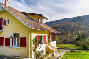 A yellow building with red shutters, a balcony, and a view of a green valley and hills. - 5 bedroom house in Annecy between town and countryside ⭐⭐⭐ (Seynod)
