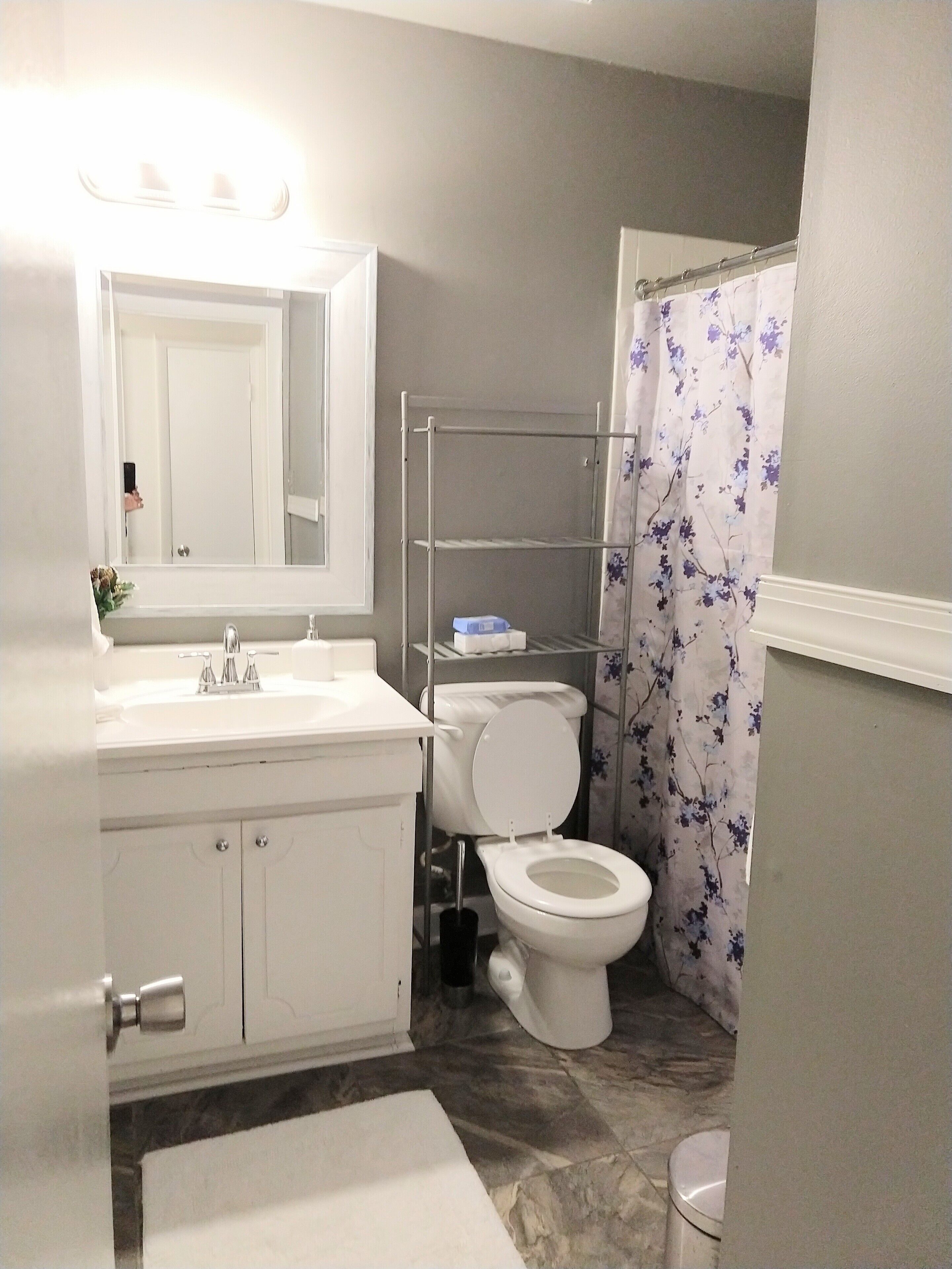 A bathroom with a white sink, mirror, and toilet. There is a shower curtain with a floral pattern.