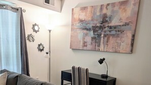 Ein Wohnzimmer mit grauem Sofa, einem kleinen Schreibtisch mit Lampe und einem großen abstrakten Gemälde an der Wand.