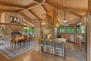 A spacious kitchen with a stone fireplace, wooden ceiling beams, and large windows. - Frank Lloyd Wright-styled Mid-Century Modern Retreat on 5 Private Acres (Rabun Gap)