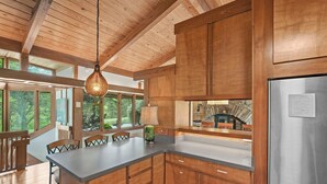 A modern kitchen with wooden cabinets, a stainless steel refrigerator, and a large island with chairs. - Frank Lloyd Wright-styled Mid-Century Modern Retreat on 5 Private Acres (Rabun Gap)