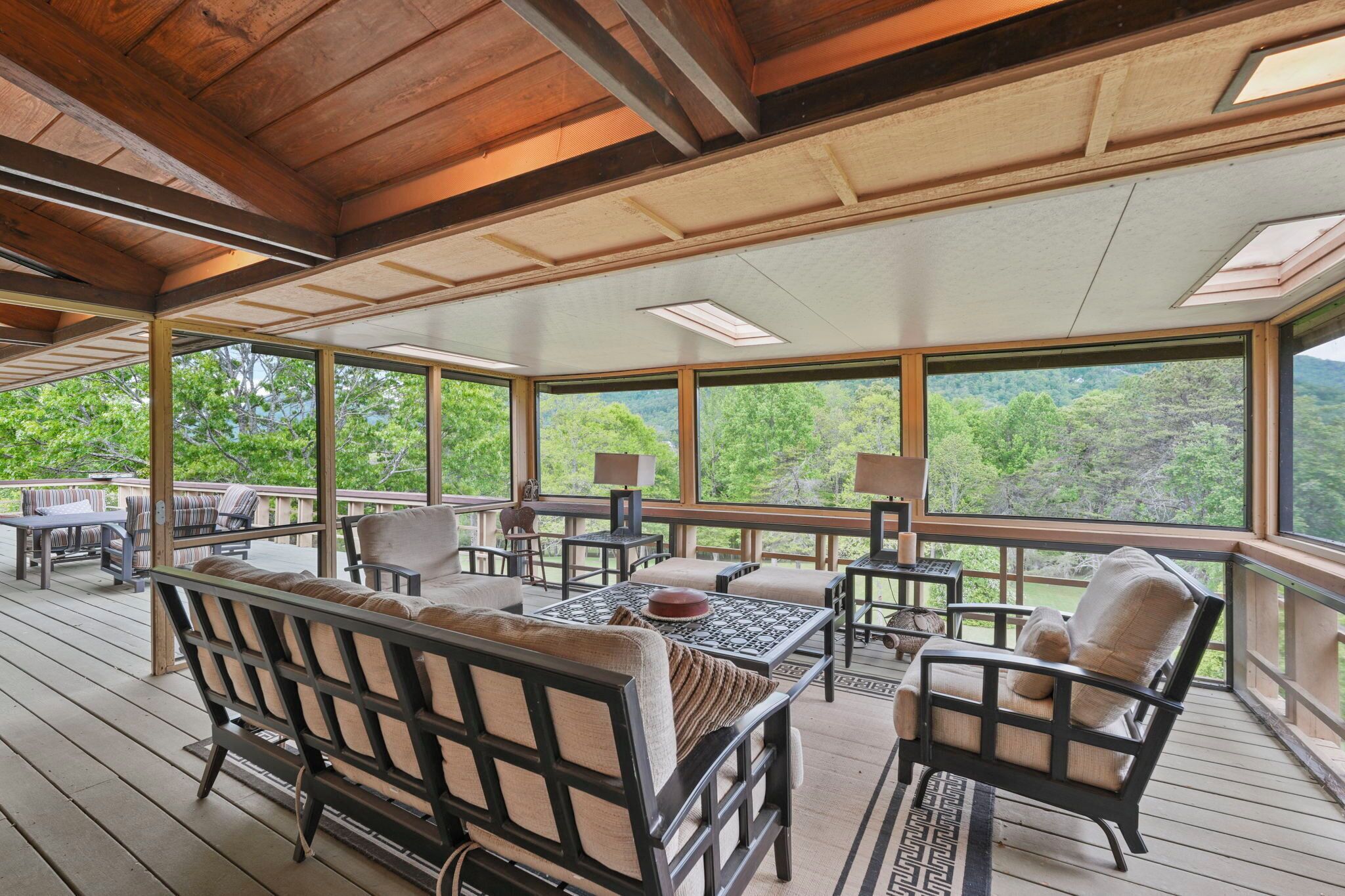 A covered outdoor deck with seating, tables, and large windows offering a view of the forest.