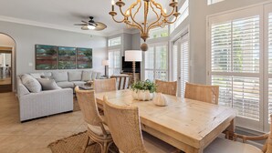 A dining area with a wooden table, wicker chairs, a chandelier, and artwork on the walls. - Serenity Now, Sandestin's Beachside, Golf Cart, Pool (Miramar Beach)