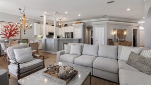 A spacious living room with a large sectional sofa, a coffee table, and a dining area with a chandelier. - Serenity Now, Sandestin's Beachside, Golf Cart, Pool (Miramar Beach)