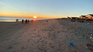 A beach with a sunset, people walking, and beach houses in the background. - Private Heated Pool and Hot Tub, across the street from the ocean! (Oak Island)