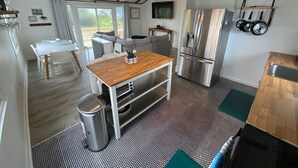 A modern kitchen with a stainless steel refrigerator, wooden table, and a large window. - Private Heated Pool and Hot Tub, across the street from the ocean! (Oak Island)