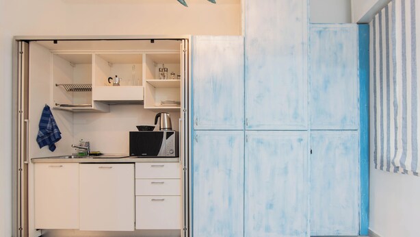 A compact kitchen with white cabinets, a black microwave, and a kettle.