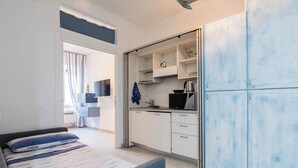 A compact bedroom with a bed, a small kitchenette, and a bathroom visible through an open door.