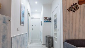 A narrow hallway with white walls, a wooden floor, and a bench on the right.