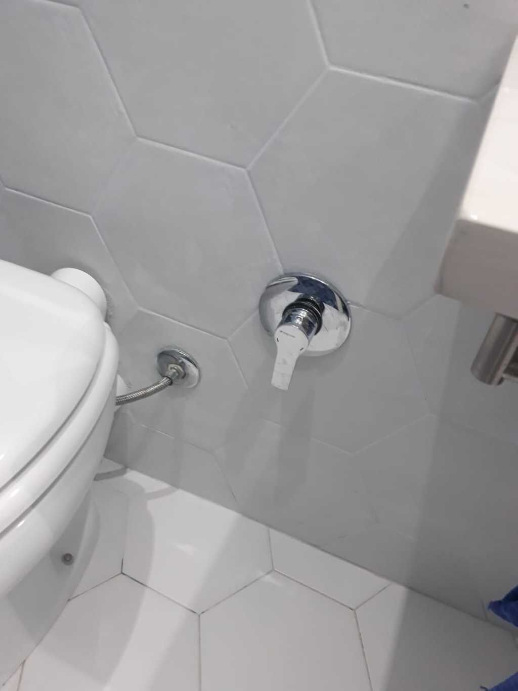 Ein Badezimmer mit einer weißen Toilette, einem Chromarmaturen und sechseckigen weißen Fliesen an der Wand.