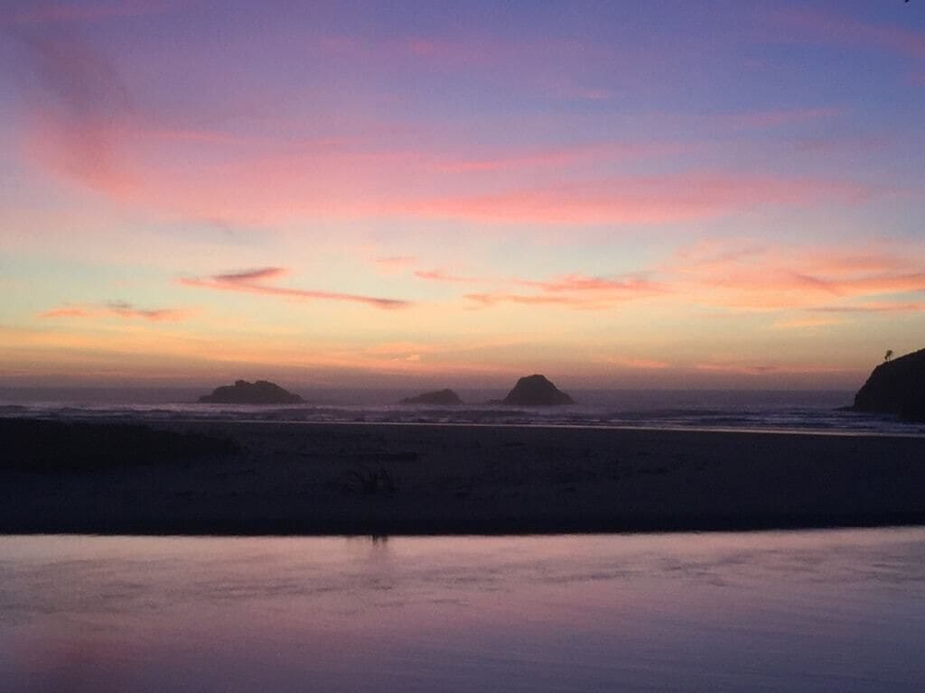 Escena de playa con agua tranquila y islas distantes bajo un cielo de atardecer colorido.