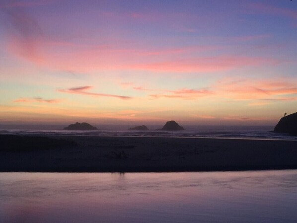 A beach scene with calm water and distant islands under a colorful sunset sky.