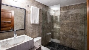 Een moderne badkamer met een marmeren wastafel, een houten kast, een douche met glazen wanden en een toilet.