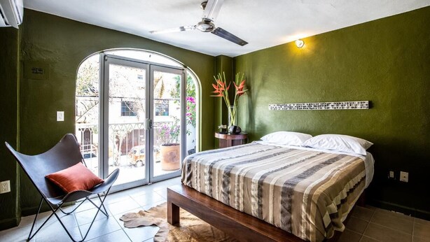 Een slaapkamer met een bed, een stoel, een plafondventilator, een raam en een wandlamp.