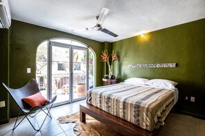 Une chambre à coucher comprenant un lit, une chaise, un ventilateur de plafond, une fenêtre et un luminaire fixé au mur.