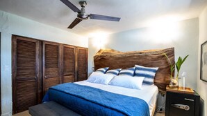 Een slaapkamer met een bed, een bankje, een nachtkastje, een plafondventilator en een kluis.