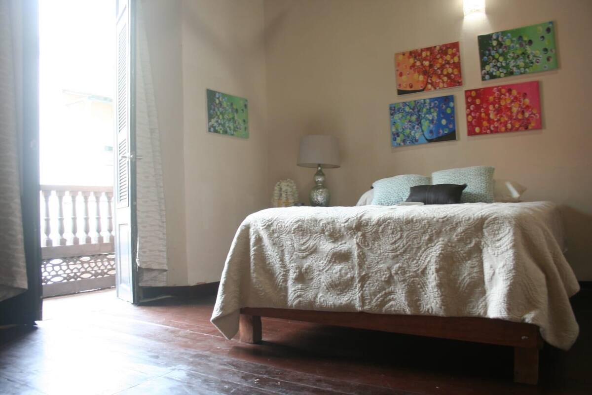 A bedroom with a bed, a nightstand, a lamp, and a balcony.