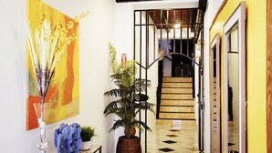 A hallway with a staircase, a large yellow wall, a painting, a potted plant, and a blue rock sculpture. - Esthelar Lodging (San Juan)