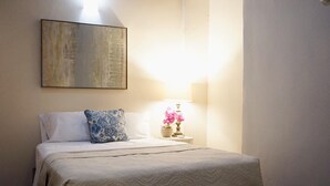 A neatly made bed with a patterned bedspread, a decorative pillow, and a bedside lamp with flowers. - Esthelar Lodging (San Juan)