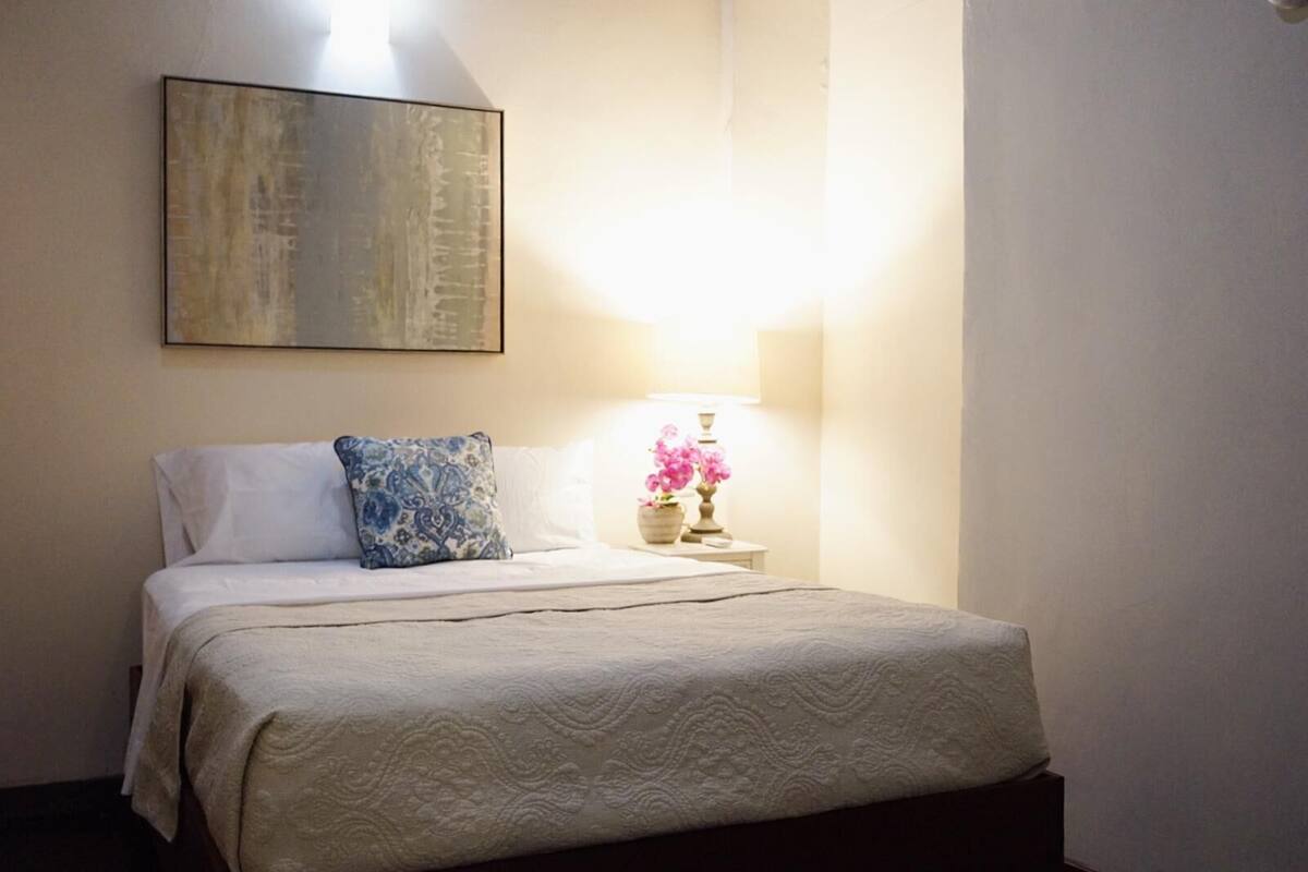 A neatly made bed with a patterned bedspread, a decorative pillow, and a bedside lamp with flowers.