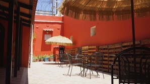 An outdoor seating area with metal chairs and a thatched umbrella, a red wall, and potted plants. - Esthelar Lodging (San Juan)