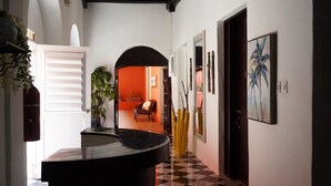 A hallway with a checkered floor, a black reception desk, a plant, and a door leading to a room with an orange wall and a chair. - Esthelar Lodging (San Juan)